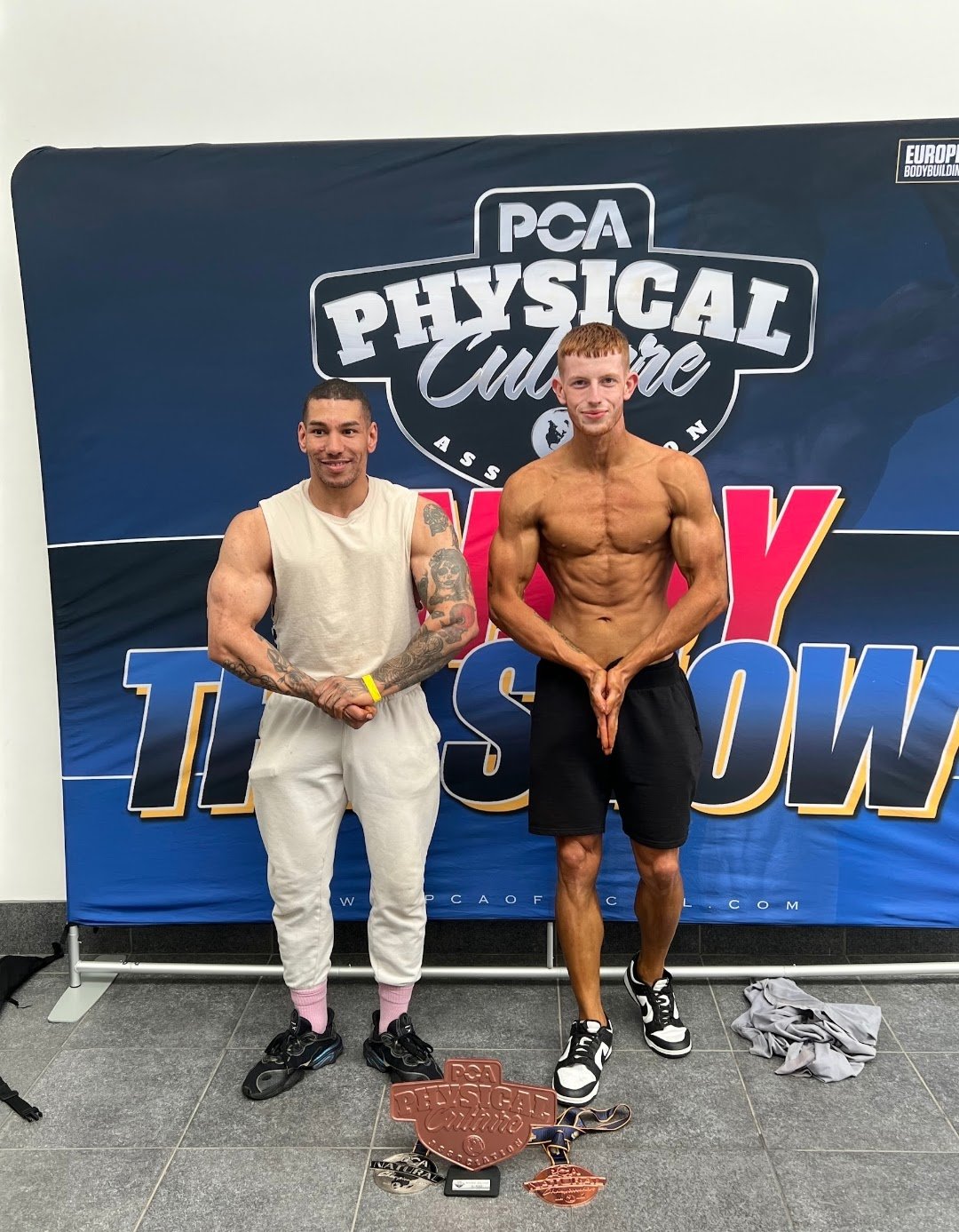 Jonny Goodall with client holding medals at bodybuilding show
